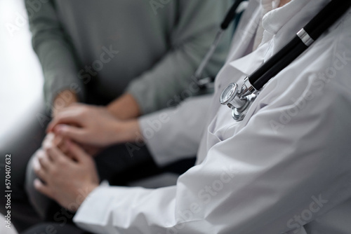 Doctor and patient sitting at green sofa. The focus is on female physician s hands reassuring woman  close up. Medicine concept