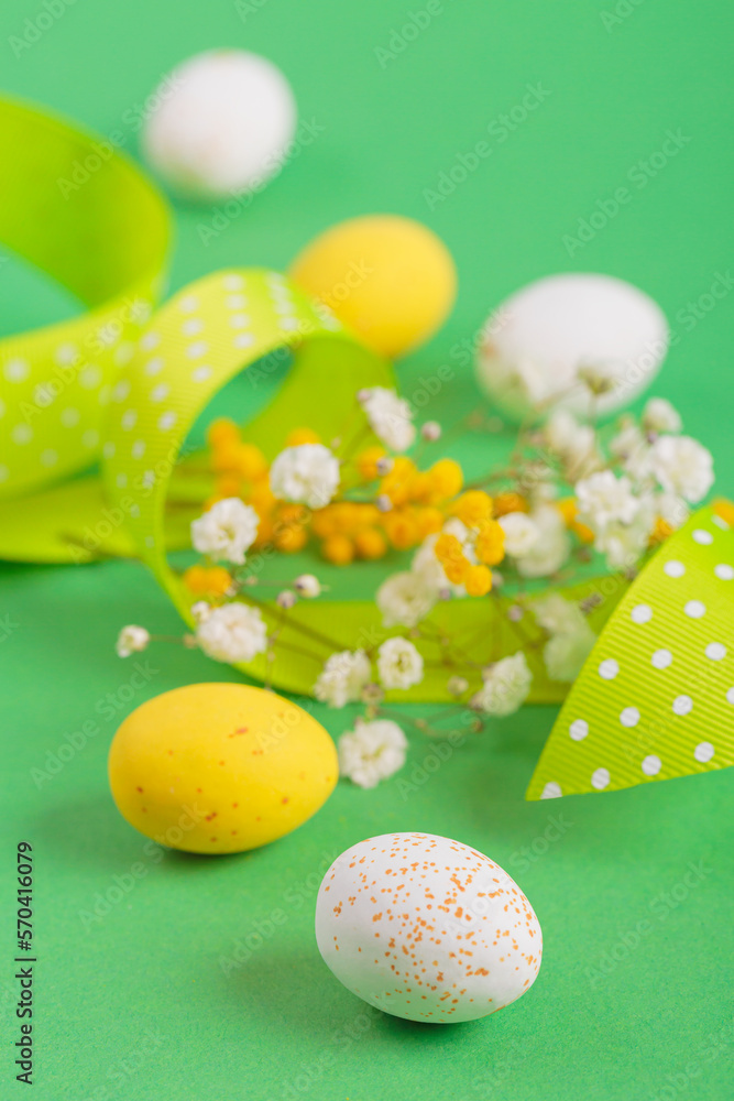 Minimalistic easter floral background made of chocolate candy eggs, flowers and ribbon on green background