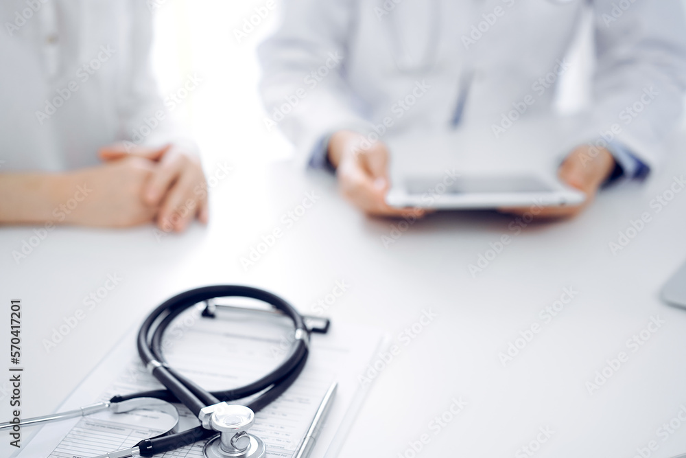 Stethoscope lying on the tablet computer in front of a doctor and patient sitting near each other and using tablet computer at the background. Medicine, healthcare concept Stethoscope lying on the tablet computer in front of a doctor and patient sitting near each other and using tablet computer at the background. Medicine, healthcare concept