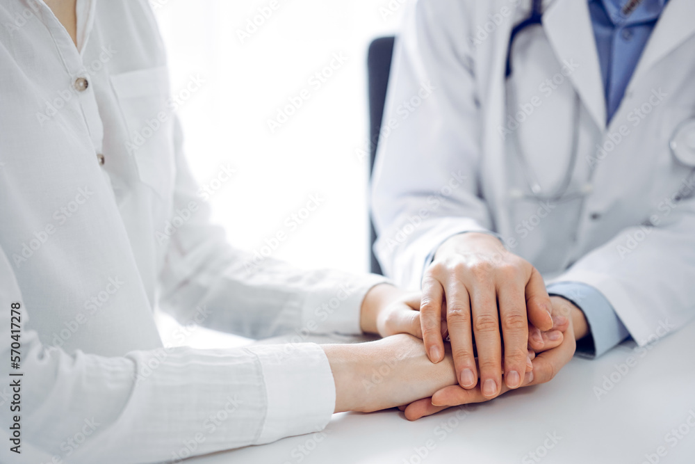 Doctor and patient sitting near each other at the table in clinic office. The focus is on female physician's hands reassuring woman, only hands, close up. Medicine concept Doctor and patient sitting near each other at the table in clinic office. The focus is on female physician's hands reassuring woman, only hands, close up. Medicine concept