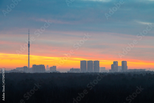 early winter dawn over dark forest and city on horizon