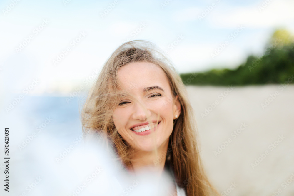 Portrait of a happy smiling woman in free happiness bliss on ocean beach enjoying nature during travel holidays vacation outdoors. View through white blurred flowers Portrait of a happy smiling woman in free happiness bliss on ocean beach enjoying nature during travel holidays vacation outdoors. View through white blurred flowers