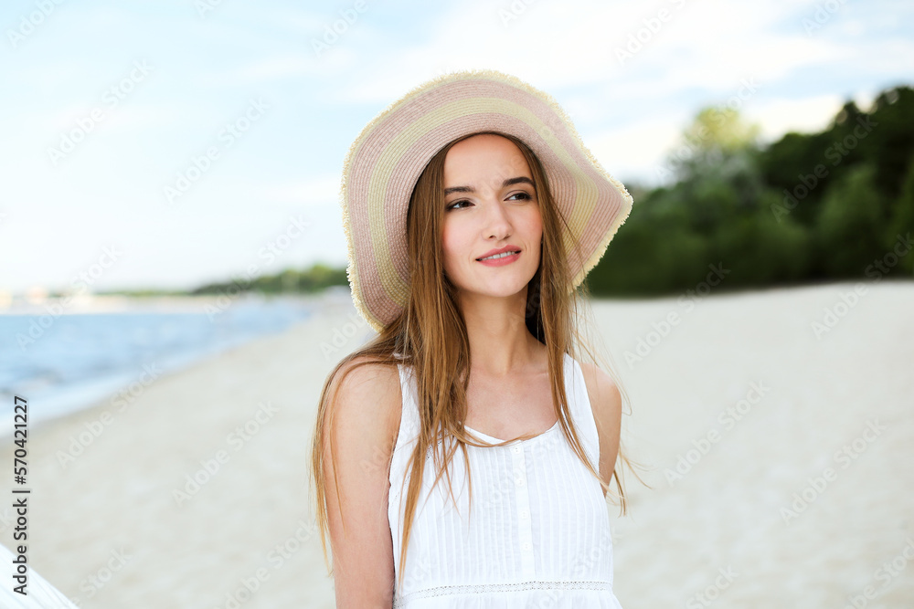 Portrait of a happy smiling woman in free happiness bliss on ocean beach standing with a hat. A female model in a white summer dress enjoying nature during travel holidays vacation outdoors