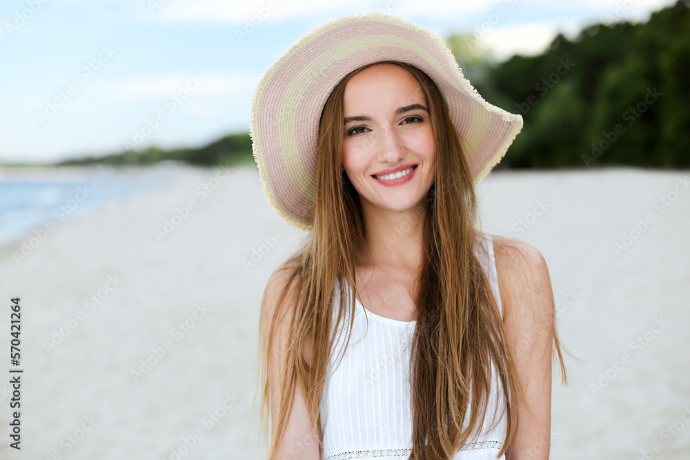 Portrait of a happy smiling woman in free happiness bliss on ocean beach standing with a hat. A female model in a white summer dress enjoying nature during travel holidays vacation outdoors