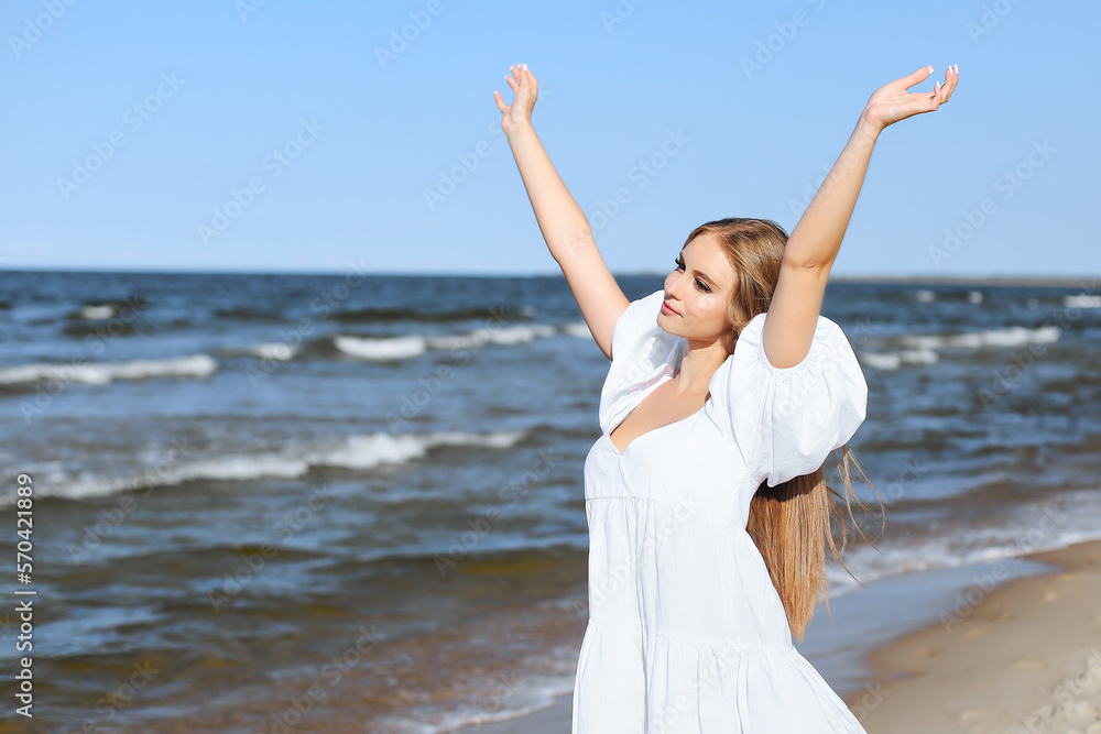 Happy smiling beautiful woman on the ocean beach standing in a white summer dress, raising hands Happy smiling beautiful woman on the ocean beach standing in a white summer dress, raising hands