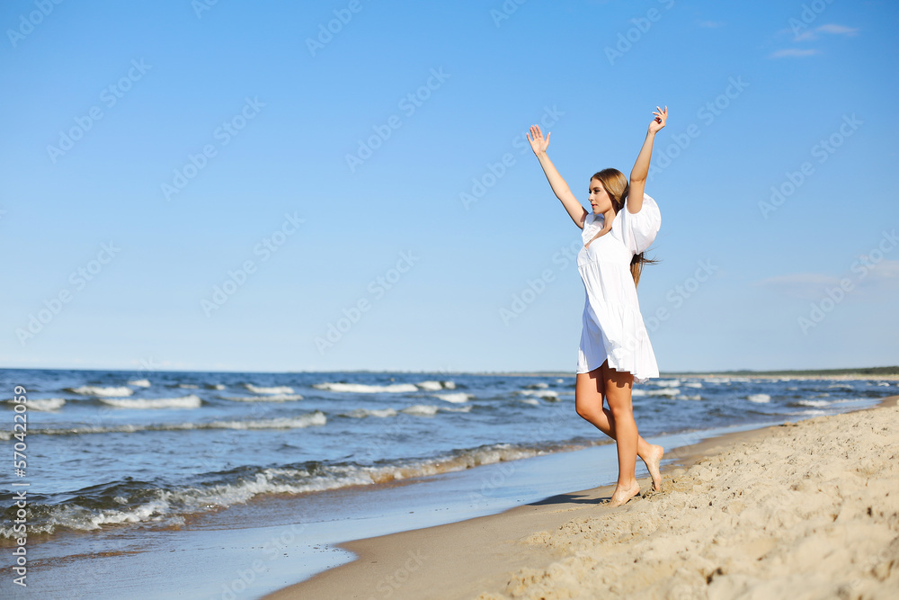 Happy, beautiful woman on the ocean beach standing in a white summer dress, raising hands Happy, beautiful woman on the ocean beach standing in a white summer dress, raising hands