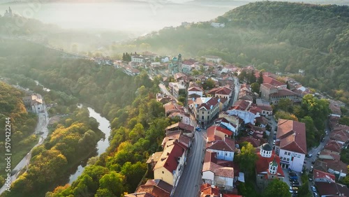 Aerial shot of sunny slightly foggy morning in Veliko Tarnovo, Bulgaria. Flying over old houses, Ascension Cathedral and river in the canyon in Veliko Tarnovo photo