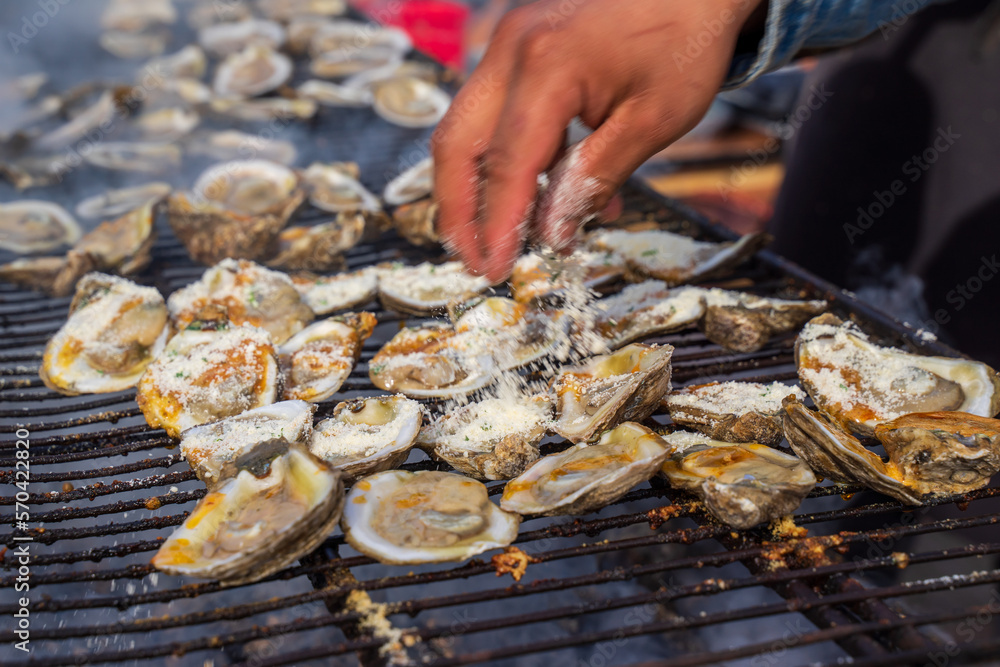Oysters are being grilled on charcoal. Oysters are open in half shelf then can be served as raw. More options for grilled with cheese topping or flake cheddar. Eat with cocktail sauce and cracker. 