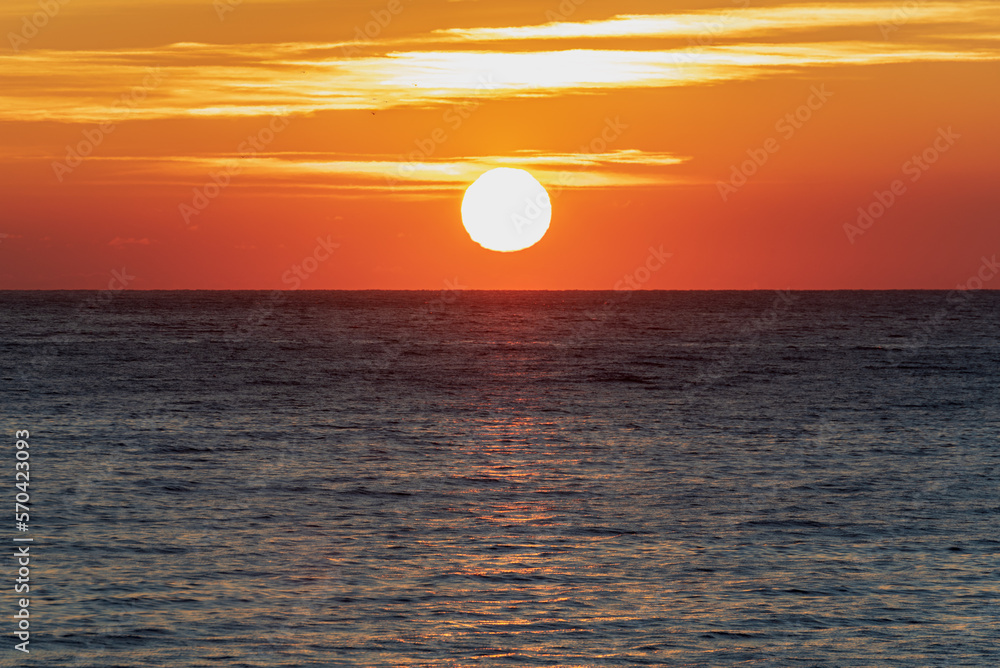 Dawn sun above the sea horizon,with orange colored sky and some clouds.