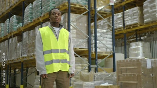 African American worker standing against racks with goods in industrial warehouse photo