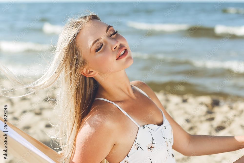 Happy blonde woman relaxing on a wooden deck chair at the ocean beach Happy blonde woman relaxing on a wooden deck chair at the ocean beach