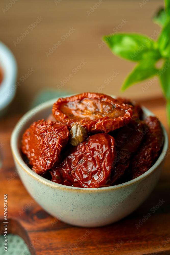 Bowl of sun dried tomatoes on wooden background.Dried tomato. Sun dried tomatoes. Infinite depth of field. Sun dried tomatoes with fresh herbs and spices. Slate background.Autumn seasonal pickled Bowl of sun dried tomatoes on wooden background.Dried tomato. Sun dried tomatoes. Infinite depth of field. Sun dried tomatoes with fresh herbs and spices. Slate background.Autumn seasonal pickled