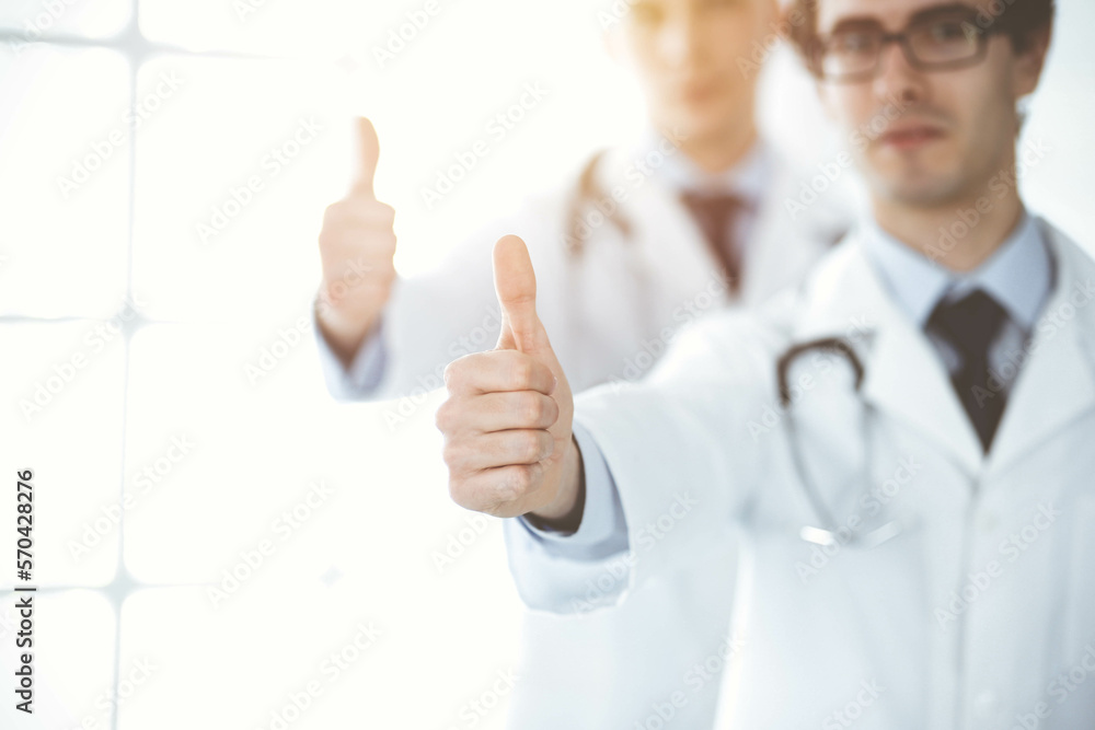 Two male doctors standing as a team and showing thumbs up as a symbol of the best service for patients in sunny clinic. Medicine concept Two male doctors standing as a team and showing thumbs up as a symbol of the best service for patients in sunny clinic. Medicine concept