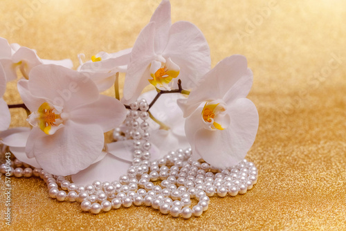 white Orchid and pearl necklace on a shiny gold background 
