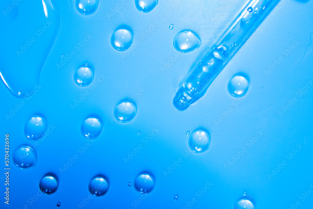 Water bubbles with cosmetic liquid drops of serum on a blue background of a laboratory glass pipette. Close-up of a pipette.