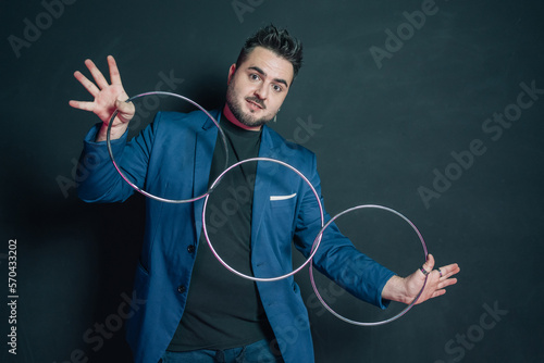 Young magician in the dark holding with both hands open a set of three linked metal rings while looking into the camera.