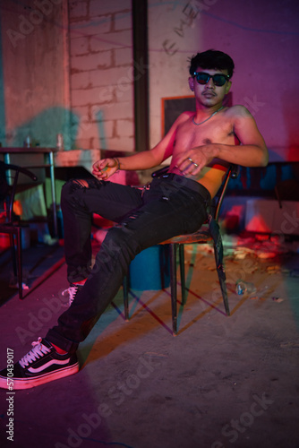 a gay man in sunglasses and denim pants sits relaxing in a club to celebrate