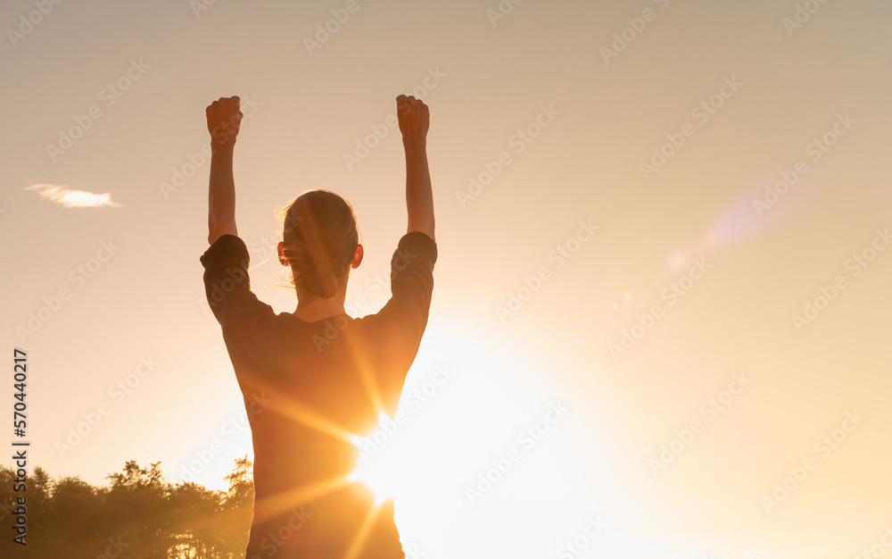 Having a strong mindset, victory and hope concept. Happy young woman with fist up facing the sunrise sky Having a strong mindset, victory and hope concept. Happy young woman with fist up facing the sunrise sky
