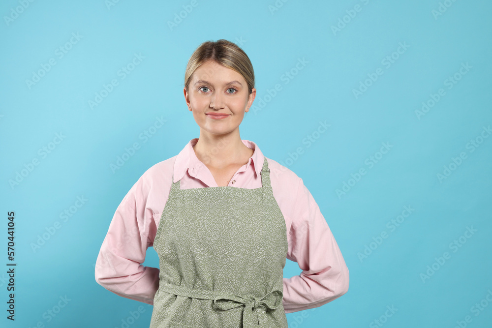 Beautiful young woman in clean apron with pattern on light blue background Beautiful young woman in clean apron with pattern on light blue background