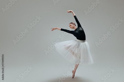 Young ballerina practicing dance moves on light grey background. Space for text