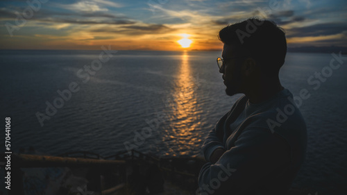 Hombre mirando el mar y el océano con el sol en el horizonte al atardecer, colores y nubes en el cielo photo