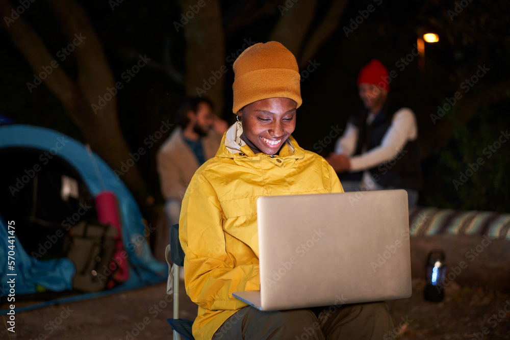 Workaholic young African girl using computer, smiling and camping winter at night. Millennial entrepreneur, typing a work email on laptop and closing a deal. Making the most of free time on vacation.