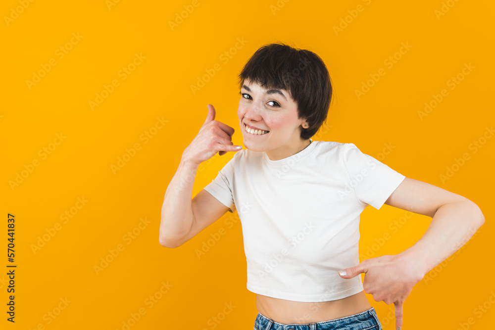Laid-back boyish-looking girl posing to the camera with a smile and doing Shaka sign. Medium studio shot over orange background. High quality photo Laid-back boyish-looking girl posing to the camera with a smile and doing Shaka sign. Medium studio shot over orange background. High quality photo
