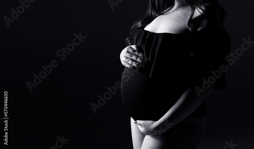 Studio pregnancy photo shoot. Silhouette of a pregnant woman on a black background with a place for text. Black and white photo.