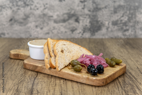 Tempting appetizer of pate' with cornichons and caper berries served on a wooden cutting board