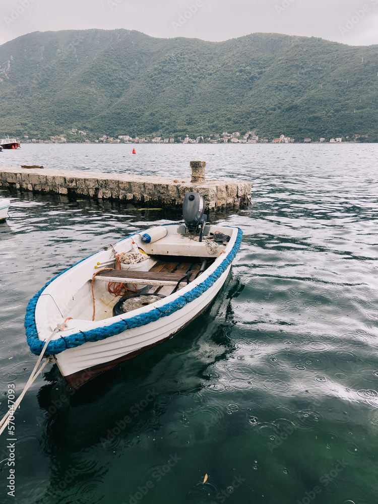 Fishing boat with a motor is moored at the pier in the rain against the backdrop of the mountains