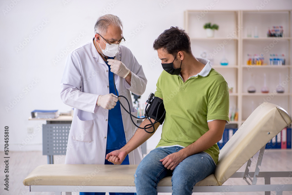 Fototapeta premium Old male doctor measuring young patient's blood pressure