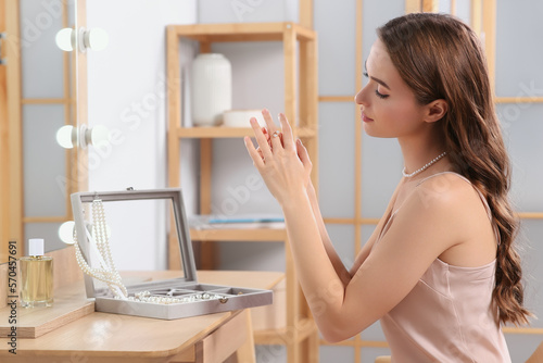 Young woman trying on elegant ring with pearls indoors photo