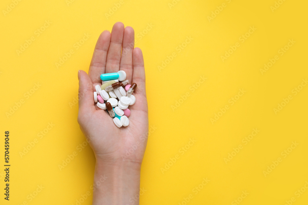 Woman holding antidepressants on yellow background, top view. Space for text Woman holding antidepressants on yellow background, top view. Space for text