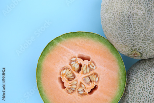 Whole and cut fresh ripe cantaloupe melons on light blue background, flat lay photo