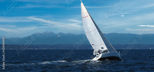 Fotografiet Isolated sailboat sailing into strong winds heeling over with speed in Elliott Bay near Seattle with Olympic Mountains in the background