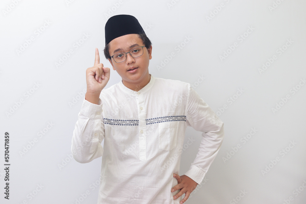Portrait of young Asian muslim man pointing up his forefinger and reminding something to do. Advertising concept. Isolated image on white background Portrait of young Asian muslim man pointing up his forefinger and reminding something to do. Advertising concept. Isolated image on white background