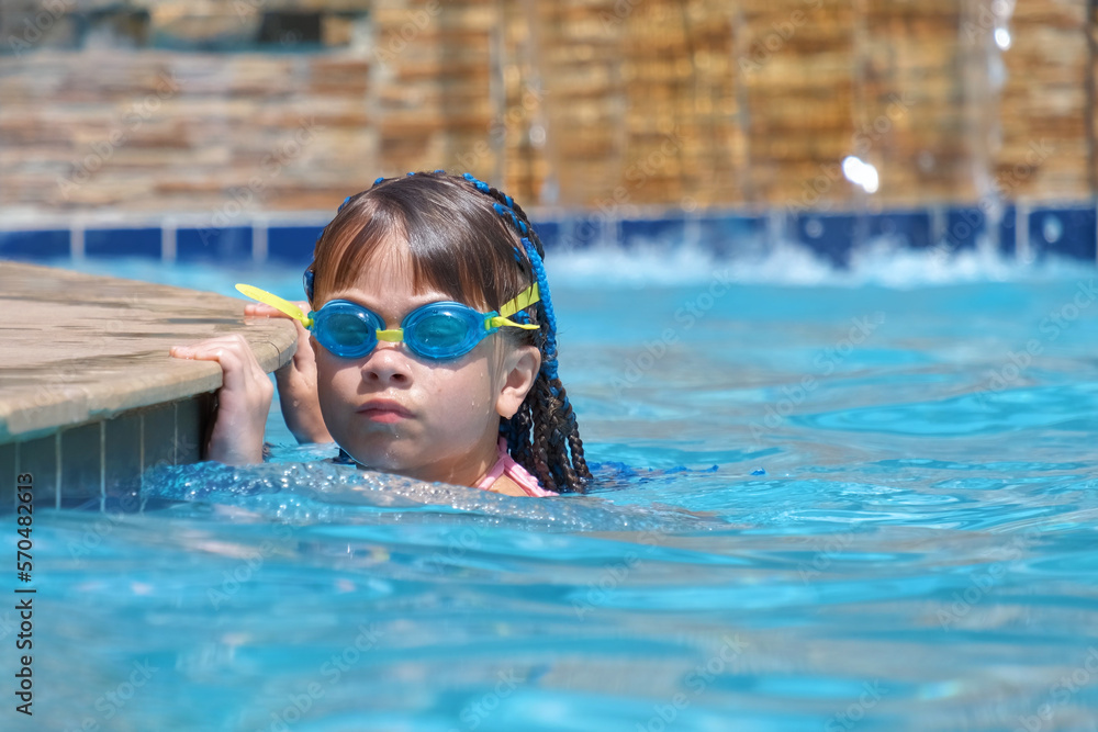 Young child girl in goggles exercises swimming in blue pool water. Summer recreation activity concept