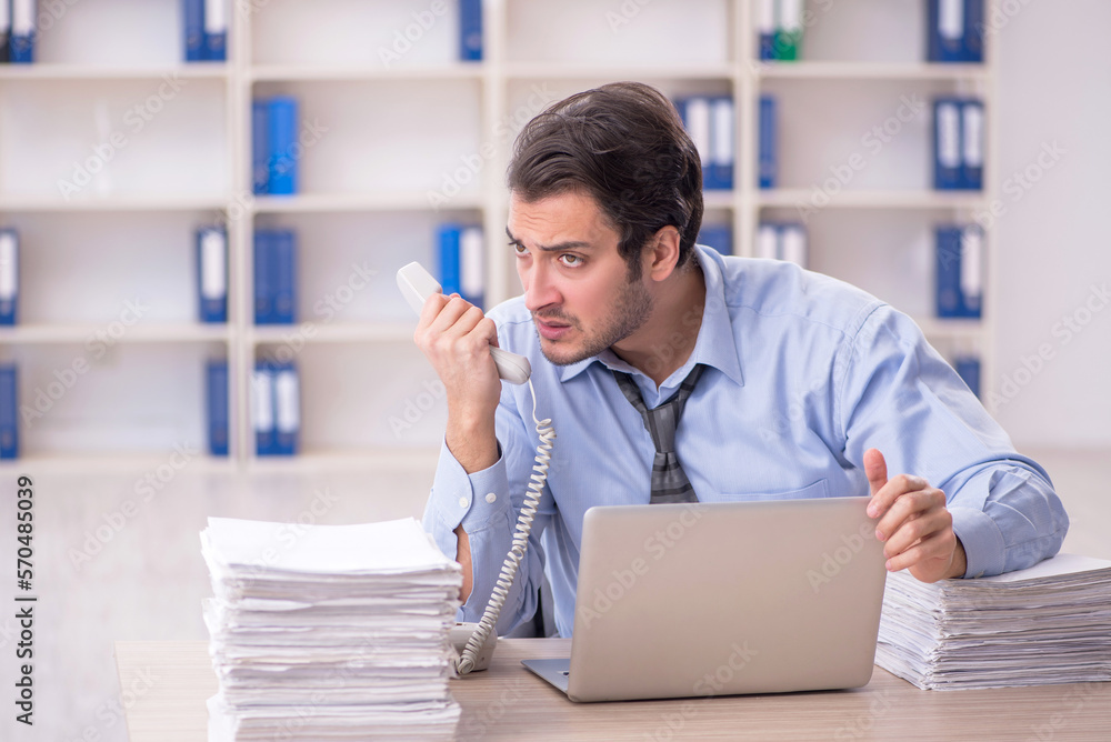 Young male employee and too much work at workplace Young male employee and too much work at workplace
