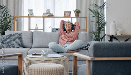 Retirement, old woman and sofa with headphones, relax and calm in living room, streaming music and audio. Female senior citizen, happy mature lady and headset for podcast, radio and carefree on couch