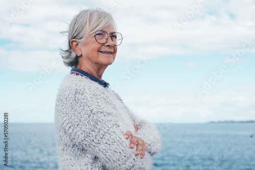 Portrait of pensive handsome senior woman standing by the sea looking away. Smiling elderly white-haired lady in outdoor excursion enjoying freedom, relax and retirement