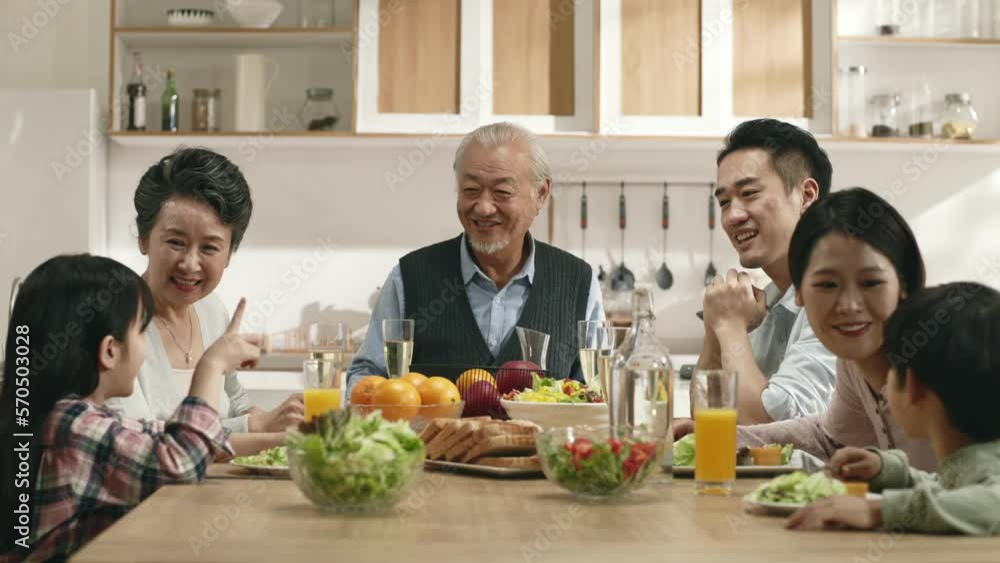 happy middle class three generation asian family sitting at table eating meal enjoying conversation happy middle class three generation asian family sitting at table eating meal enjoying conversation