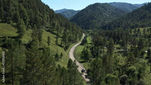 Drone follow shot white automobile roof box route travel journey mountain river pond with trees forest summer aerial view shot. White SUV car riding gravel road cinematic natural tourism vacation 4k