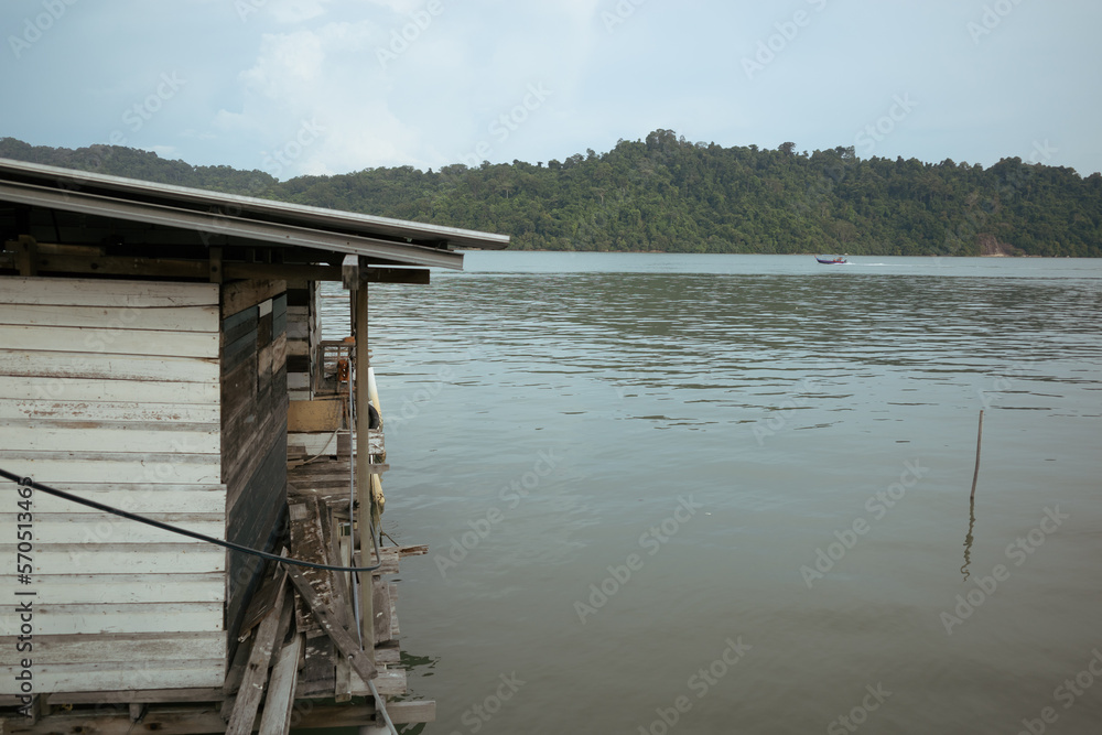 A Malaysian house on stilts sitting on top of a body of water. It is built with planks and zinc roof