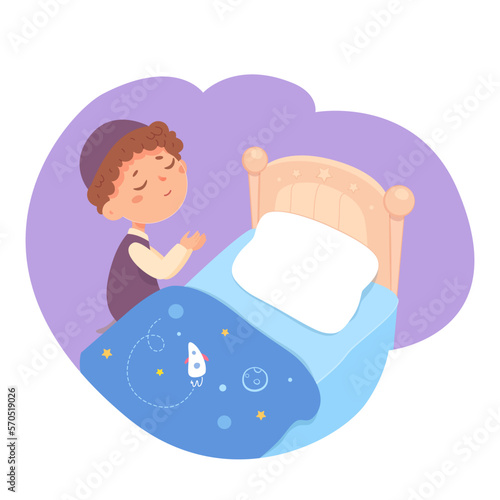 Child praying in bedtime, cute boy kneeling beside bed, little kid holding hands up