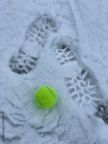 Foot prints on the fresh snow and a lost tennis ball. Winter sport tennis. © Tetiana