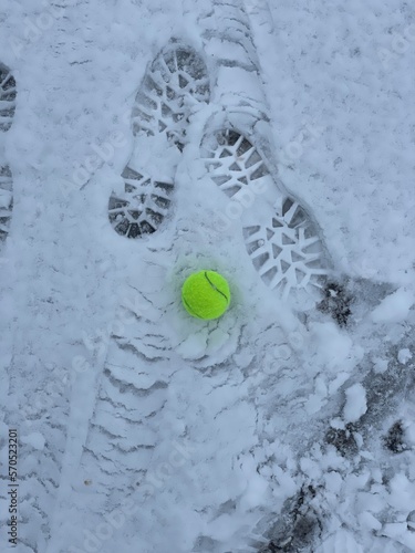 Foot prints on the fresh snow and a lost tennis ball. Winter sport tennis.