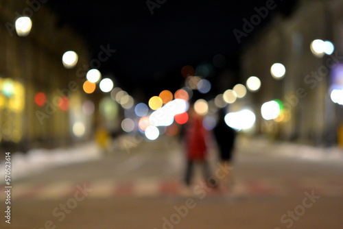 Blurred background. Night city. Blurred silhouette of buildings, bokeh spots of glowing lanterns, blurred silhouettes of people walking on the street in the evening. City square, black night sky © mari1408