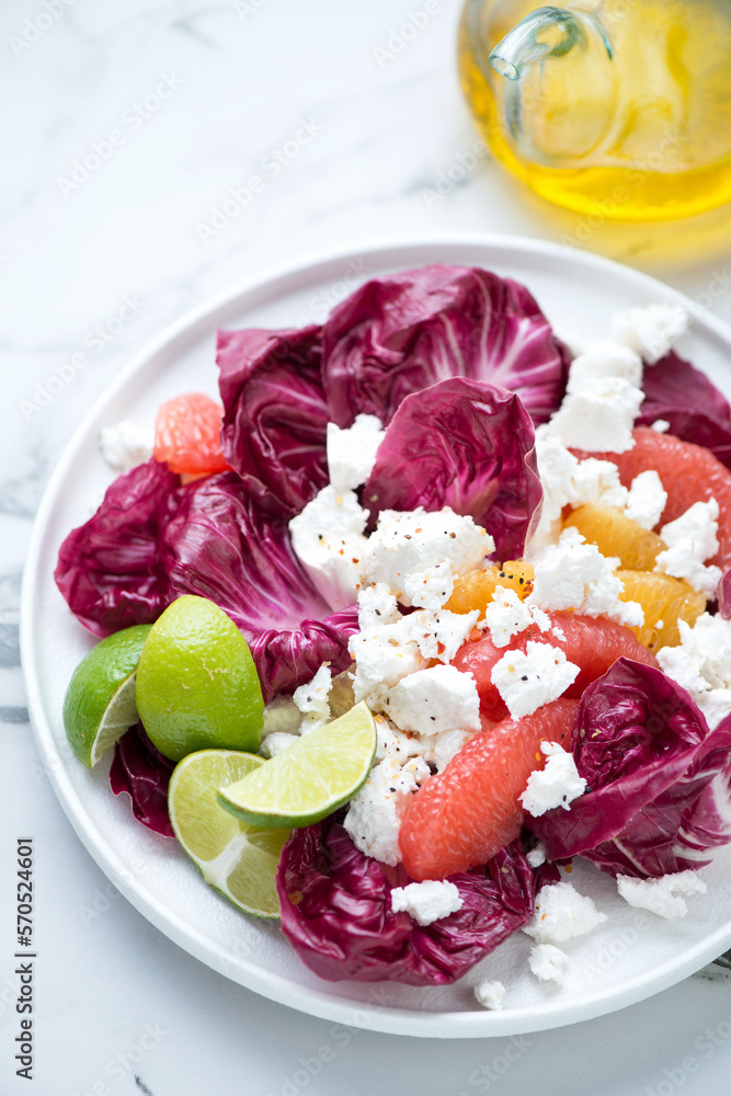 Salad with radicchio, grapefruit, orange and goat cheese, vertical shot on a white marble background, middle closeup