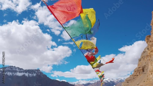 4K shot of colorful Buddhist prayer flags fluttering in wind in background of snowy mountains and clouds in sky at Kaza, Spiti Valley, India. Prayer flags in front of the mountains during the summer. photo