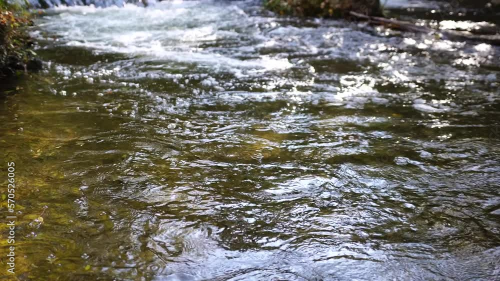 Closeup of a rushing stream, swift flow of spring water with some autumn colourful leaves in the water. Grey big stones, fallen autumnal leaves. Waterfall at fall. Nature's landscape. Slow motion Closeup of a rushing stream, swift flow of spring water with some autumn colourful leaves in the water. Grey big stones, fallen autumnal leaves. Waterfall at fall. Nature's landscape. Slow motion